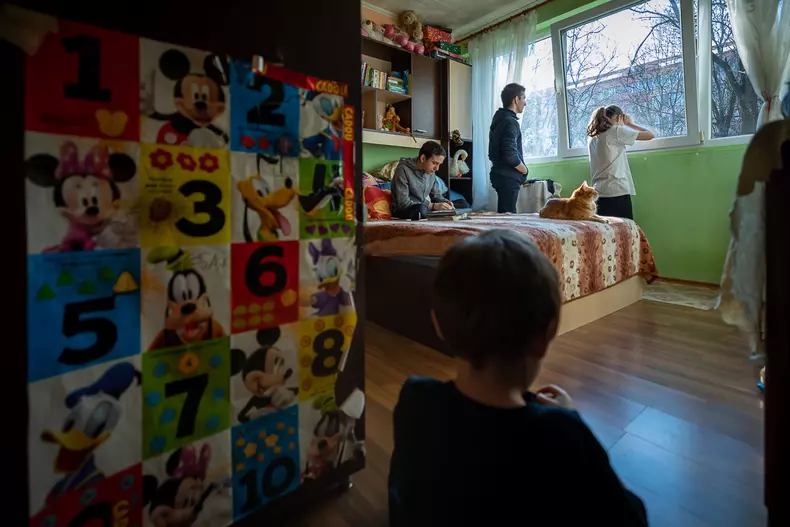 Mihai și Irina se uită pe geam la alți copii care au ieșit afară în parcul din fața blocului.