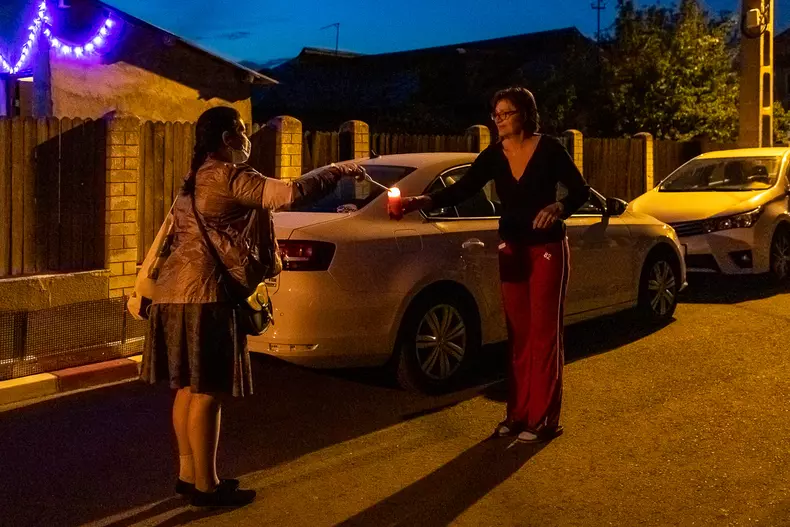 O femeie din Voluntari ia lumină de la o voluntară, încercând să păstreze recomandările de distanțare socială. Foto Eli Driu