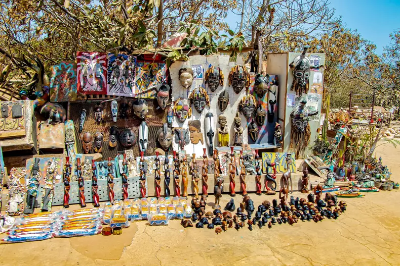 Gorée island, Senegal- April 22 2019: Beautiful wooden colorful dolls, figurines and masks with typical Senegalese drawings and baobab seeds. It is a local art in Africa.