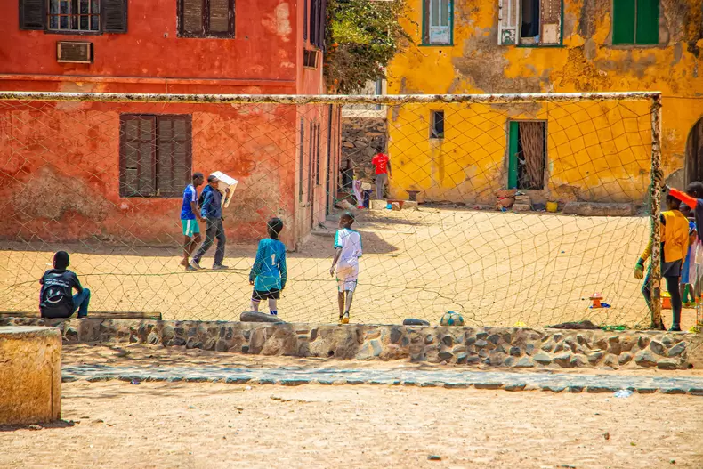 Goree island, Senegal- April 22 2019: Unidentified boys play soccer on the sand in the town in Africa. oys playing in front of an old yellow house on a football field.
