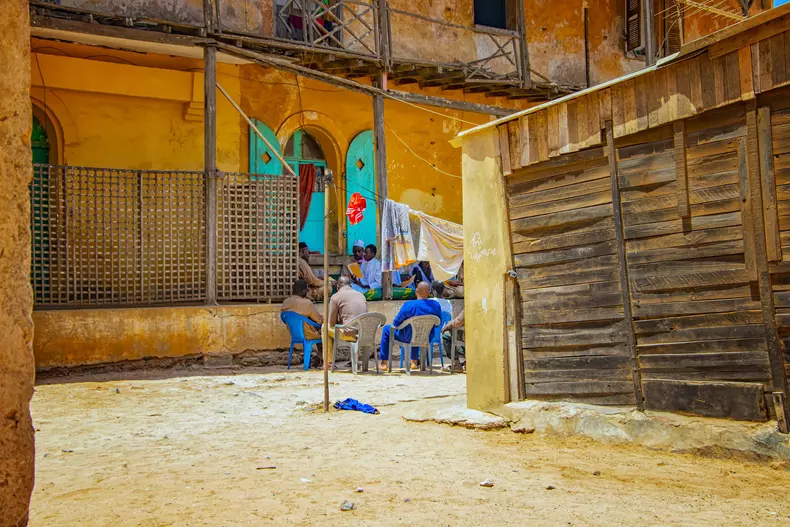 GOREE/SENEGAL - April 22, 2019: A group of senegalese men sitting and chatting on a dusty street at Goree island, Dakar, Senegal. One man reads from a book.