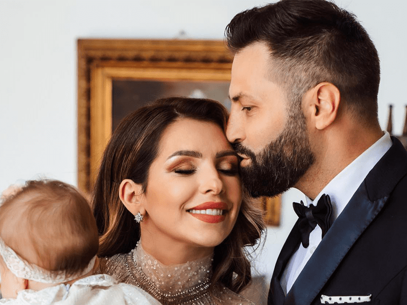 Celia este sărutată pe frunte de soț în timp ce ține un copil în brațe.