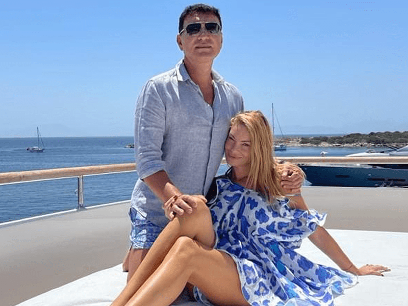 Cristi Borcea îmrăcat într-o cămasă și pantaloni scurți o ține de umăr pe soția sa , Valentina îmbrăcată într-o rochie alb cu albastru.