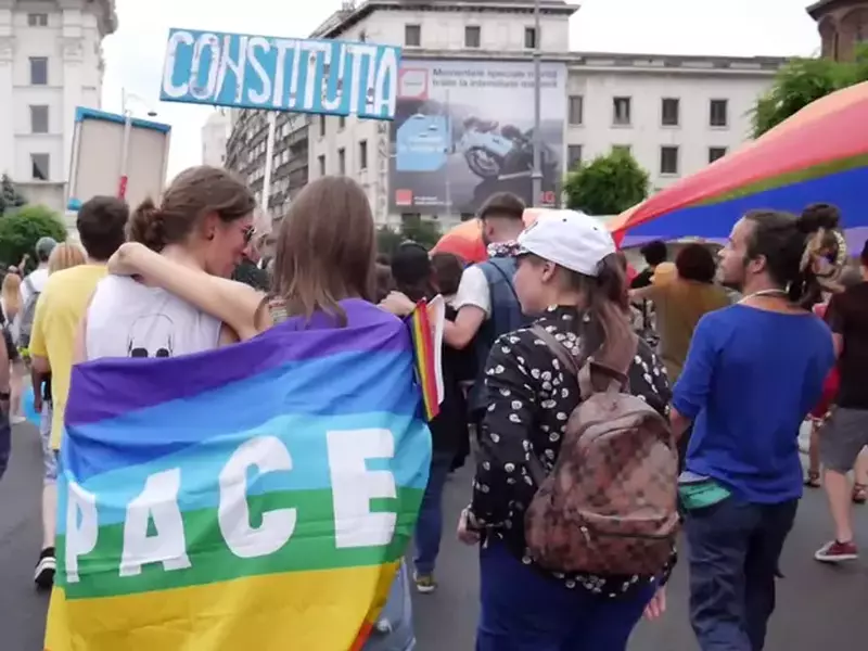marșul gay din București. Două fete purtând pe spate un steag pe care scrie PACE