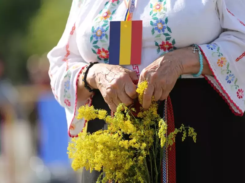 O bâtrână îmbrăcată în ie, cu un mic tricolor la gât