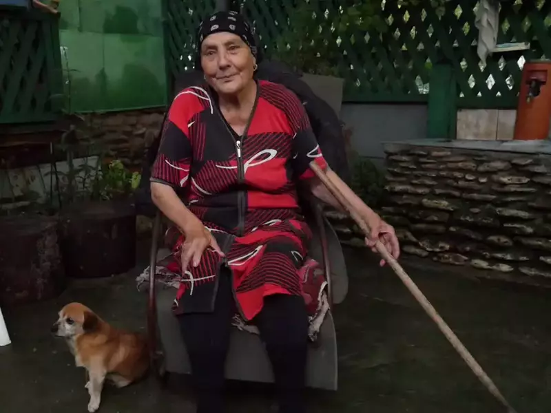 Localnicii din Vama Veche. Sultana Dumitrache, stând pe scaun, în curte, cu un cățel la picioare