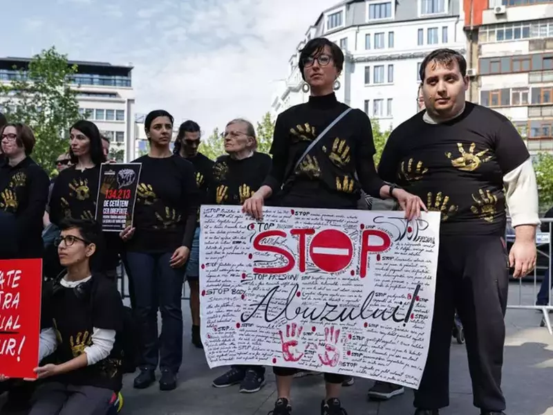 tineri care țin bannere roșii și albe, îmbrăcați în haine negre acoperite de urme de palme aurii, care participă la protestul pentru soluționarea dosarului deschis în urma violului unei minore la școala de vară AUR, în fața Parchetului de pe lângă Curtea de Apel București, 14 mai 2025