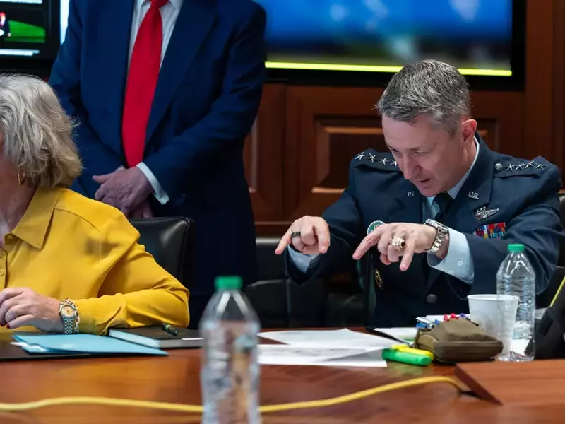 Susie Wiles (stânga) și Dan Caine (dreapta) surprinși în Situation Room pe 21 iunie 2025. Wiles poartă o bluză de culoarea muștarului și privește în stânga, în timp ce Caine privește în jos și ține mâinile ridicate deasupra mesei