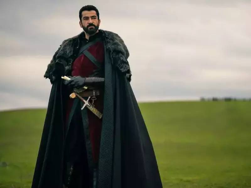 Fotografie artistică , scena de film cu actorul Kenan İmirzalıoğlu, imbracat ca un războicuc, cu pelerina si sabie la brâu, în natură, pe un camp verde si cu un cer innorat