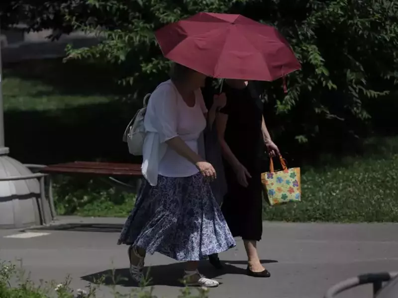 Două femei merg prin parc într-o zi caniculară de vară și se protejează de soare cu o umbrelă vișinie, București, 16 iulie 2025