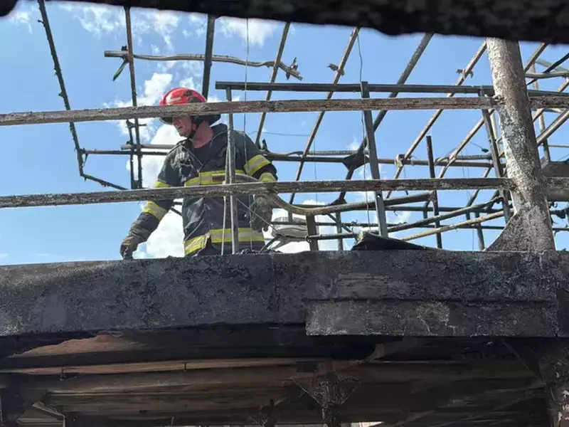 Un pompier, îmbrăcat în uniformă de intervenție ignifugă, de culoare neagră cu benzi reflectorizante verzi și o cască de protecție roșie, văzut de jos, printr-un cadru metalic afumat în cadrul incendiului de la pontonul dormitor din Tulcea, 3 august 2025