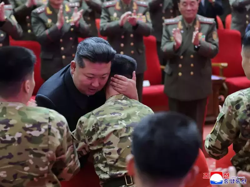 Kim Jong-un, îmbrăcat într-un costum negru, îmbrățișează un soldat în fața fotografiilor cu soldații morți în Kursk în timpul unei vizite la zidul memorial în cadrul unei ceremonii de decernare a distincțiilor de stat comandantului și combatanților Forțelor Operaționale de peste hotare ale Armatei Populare Coreene, care au participat la operațiuni militare în regiunea Kursk din vestul Rusiei, la sediul Comitetului Central al Partidului Muncitorilor din Coreea (WPK) din Phenian, 22 august 2025