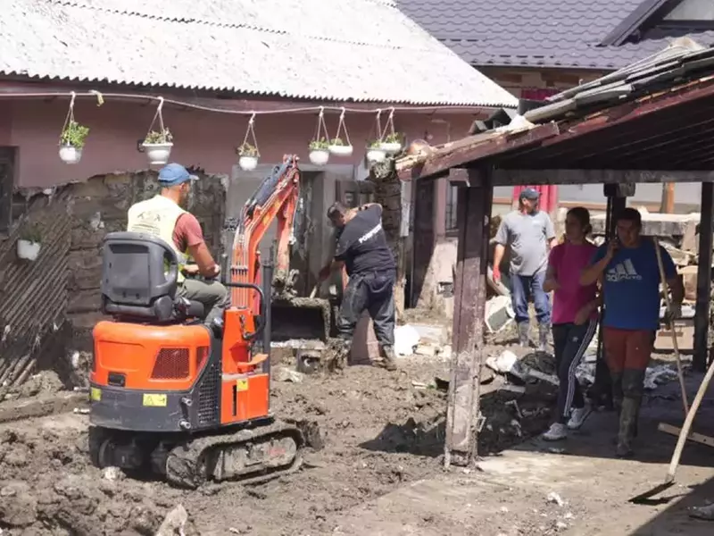 Voluntarii și pompierii lucrează cu un excavator pentru a scoate noroiul dintr-o curte din Broșteni