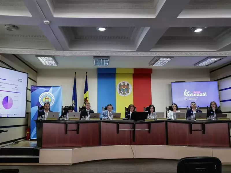 mai multi mebri ai Comisia Electorală Centrale din Chișinău stau la prezidiu la o masa semicirculara. In spatele lor se observa mai multe plasme cu date despre alegeri si un drapel mare al tarii