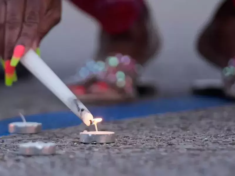 Mana unei femei cu o lumanre, care aprinde o alta lumanare, la locul atacului armat în masă, duminică, 19 aprilie 2026, în Shreveport, Louisiana.