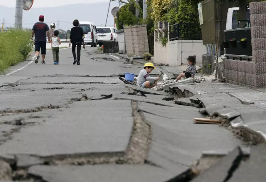 epaselect epa05261226 A boy and his younger sister play amid cracks in a road in front of their house following a second powerful earthquake, in Mashiki, Kumamoto Prefecture, southwestern Japan, 16 April 2016. A 7.3 magnitude earthquake that struck southwestern Japan early 16 April has now left 19 dead and a thousand injured, in a region where a day before another powerful quake claimed ten lives. The latest quake occurred on Kyushu island's western coastal prefecture of Kumamoto, with an epicenter located about 10 kilometers deep. EPA/KIMIMASA MAYAMA