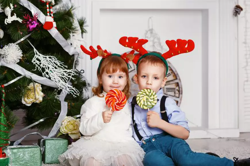 49810332 - little girl and boy in reindeer antlers eating a lollipops. portrait of two funny little kids with a delicious candies in the hands. christmas and new year concept. happy children and family in anticipation of the new year and christmas.