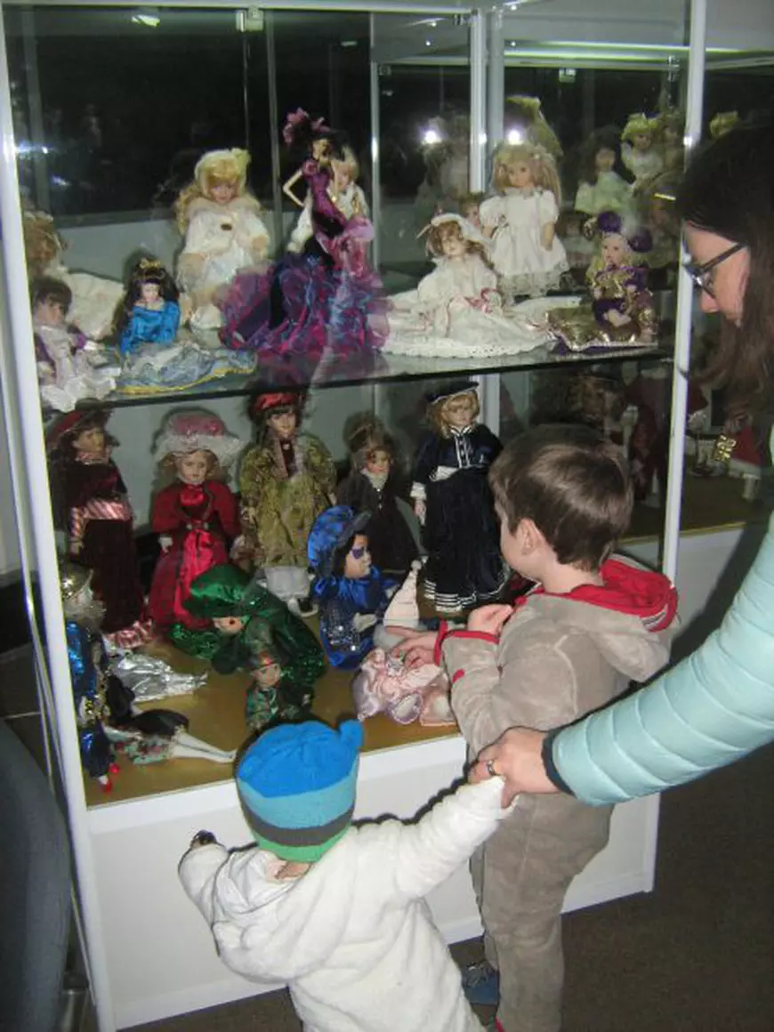 doi copii împreună cu mama lor admiră o colecție de păpuși de porțelan