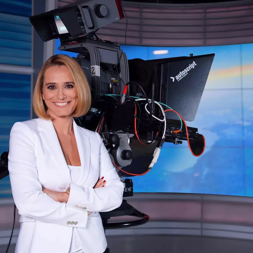 Andreea Esca, zâmbitoare lângă o cameră de televiziune, în platoul Știrilor Pro TV