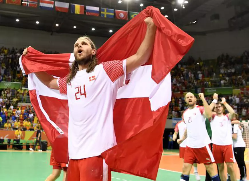 epa05505451 Mikkel Hansen of Denmark carries the Dannebrog as he celebrates their win in the men's Handball Gold Medal match of the Rio 2016 Olympic Games between Denmark and France at the Future Arena in the Olympic Park in Rio de Janeiro, Brazil, 21 August 2016. EPA/MARIJAN MURAT