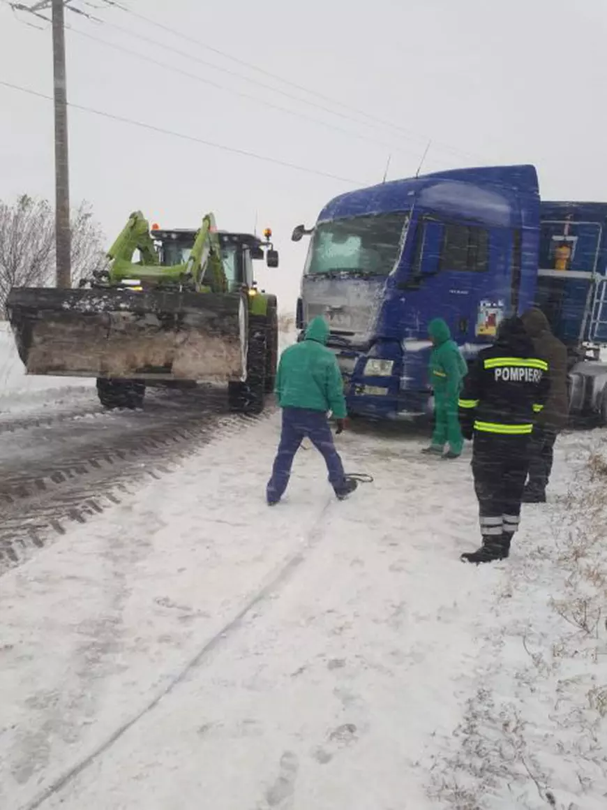 Camion blocat în zăpada. Lângă el se află angajați de la Drumuri și un pompier, alături de un excavator