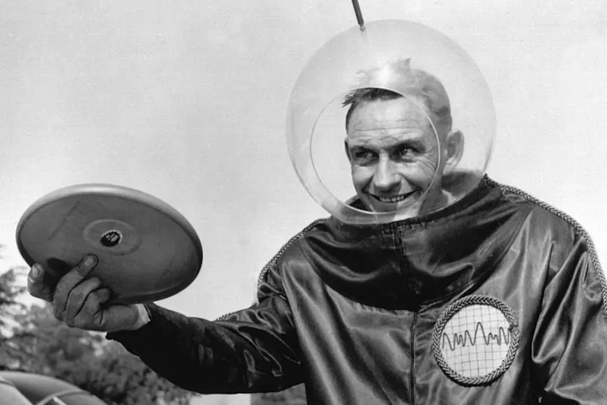 Istoria Frisbee – Imagine cu inventatorul Friesbee, Walter Frederick „Fred” Morrison, în costum de astronaut, ţinând discul în mână.
