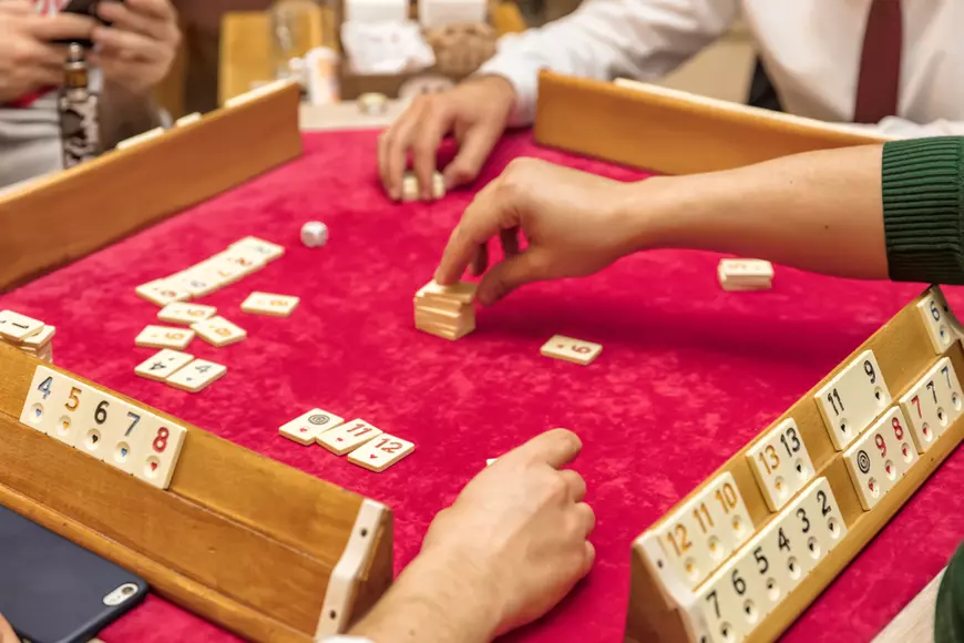 Cum se joacă remi – reguli de bază și sfaturi utile pentru jucători - Patru persoane joacă remi la o masă acoperită cu catifea roşie.