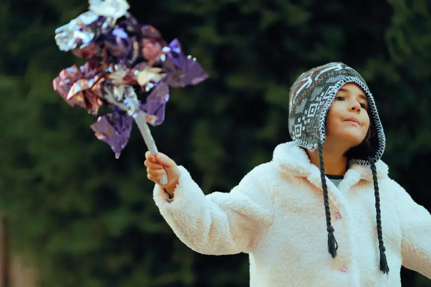 O fetita, imbracata cu o haina alba si cu caciula pe cap, a plecat la colindat tinand in mana o sorcova