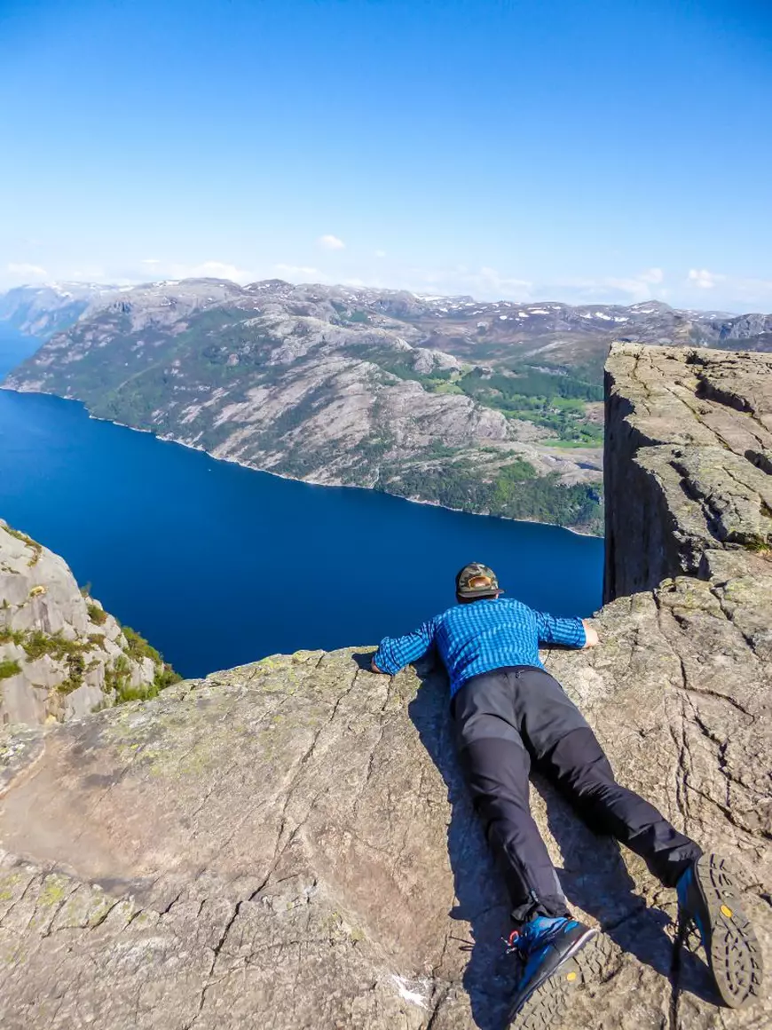 Ce este acrofobia - Imagine cu un bărbat aflat pe un munte şi aşezat pe burtă, care piveşte în jos, de la mare înălţime, spre un lac.