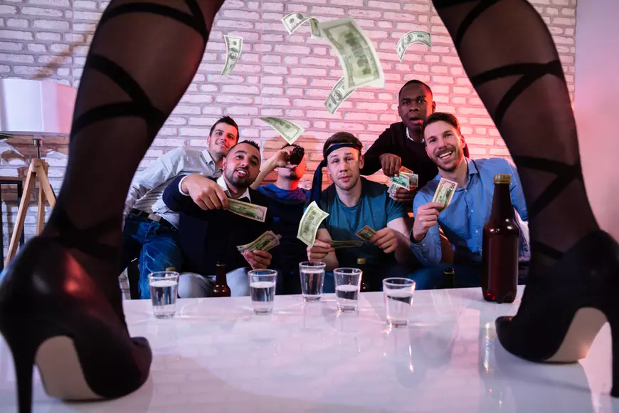 Ghid pentru organizarea unei petreceri a burlacilor - Imagine cu un grup de bărbaţi care urmăresc o tânără care dansează pe o masă.