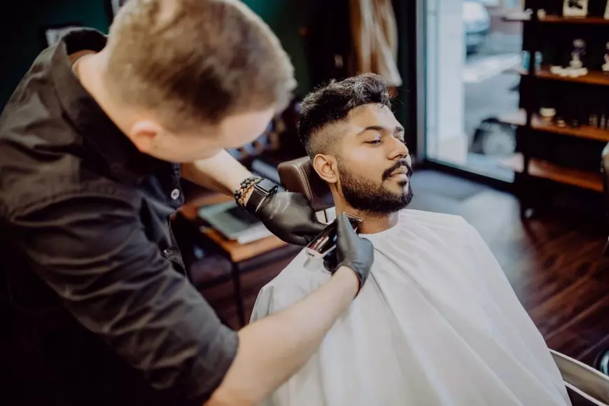 De ce îşi lasă bărbaţii barbă - Imagine cu un frizer care îi tunde barba unui tânăr.