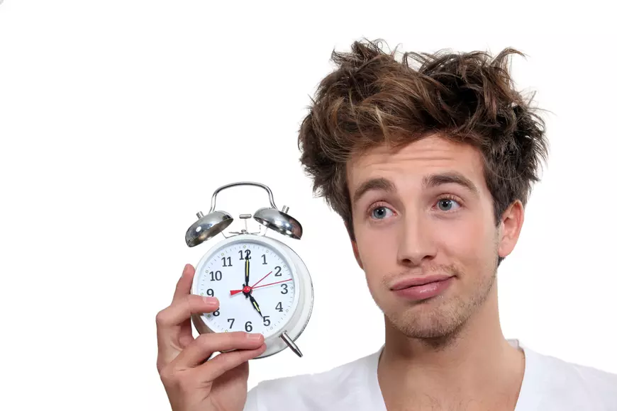 Beneficii ale trezitului devreme - Bărbat care ţine în mână un ceas deşteptător, care arată ora 05.00, sugerând că s-a trezit foarte devreme.