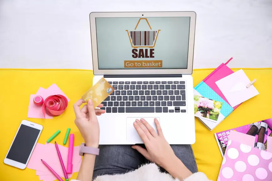 Care este momentul potrivit al anului să cumperi diferite lucruri - Imagine cu o tânără care îşi ţine laptopul pe genunchi şi încearcă să profite de reducerile dintr-un magazin online.