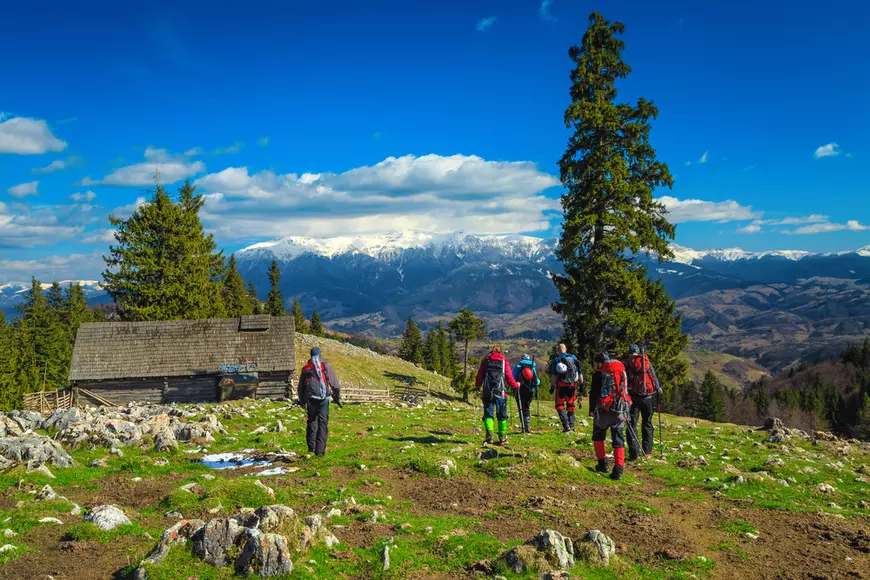Ce reguli trebuie să respecţi când mergi la munte - Imagine cu un grup de turişti care se îndreaptă către o stână, pe munte.