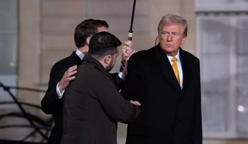 donald trump imbracat cu o camasa alba si palton negru in timp ce da mana cu volodimir zelenski. in spatele lor este emanuel macron