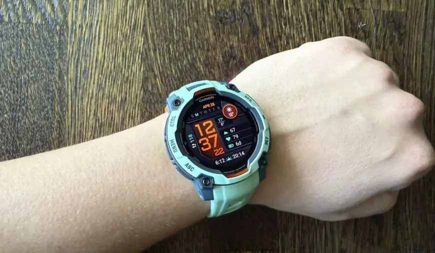 Ceas Garmin Instinct 3 AMOLED, de culoare turcoaz, la încheietura unui bărbat, așezată pe un fundal de lemn.