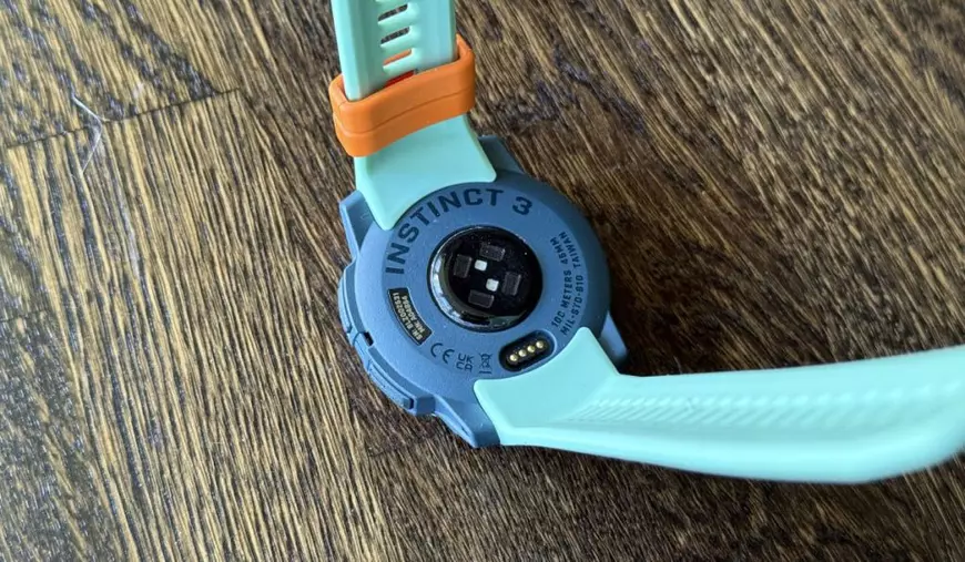 Ceas Garmin Instinct 3 AMOLED, de culoare turcoaz, așezat pe un fundal de lemn.