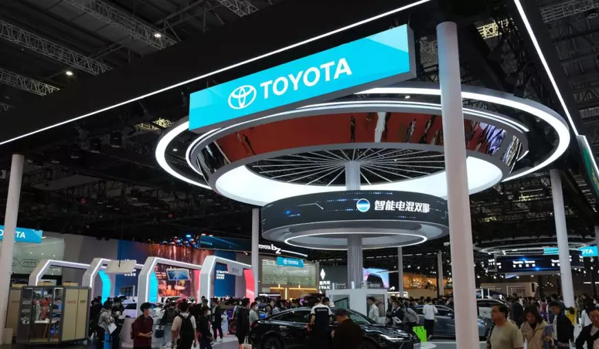Stand al companiei Toyota la un târg internațional auto din China cu ecrane LED care afișează logo-ul Toyota și mesaje în limba chineză. În mijlocul standului se află o mașină neagră de prezentare