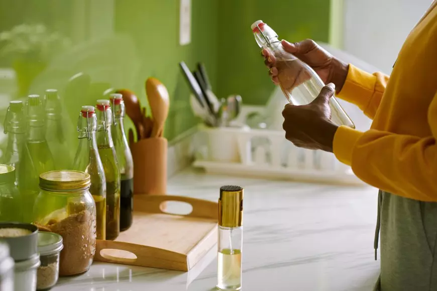 Care este diferenţa dintre oţet şi acid acetic alimentar - Imagine cu o persoană acre ţine în mână o sticlă cu oţet