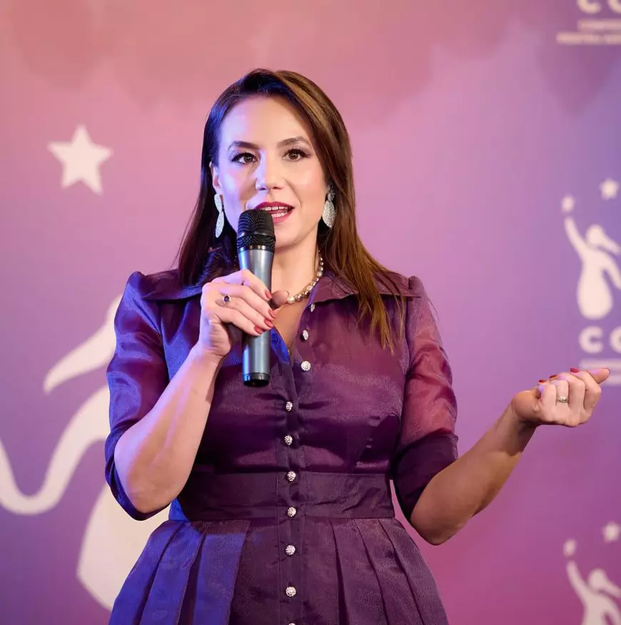 Femeie cu părul lung, îmbrăcată elegant, care vorbește la microfon 