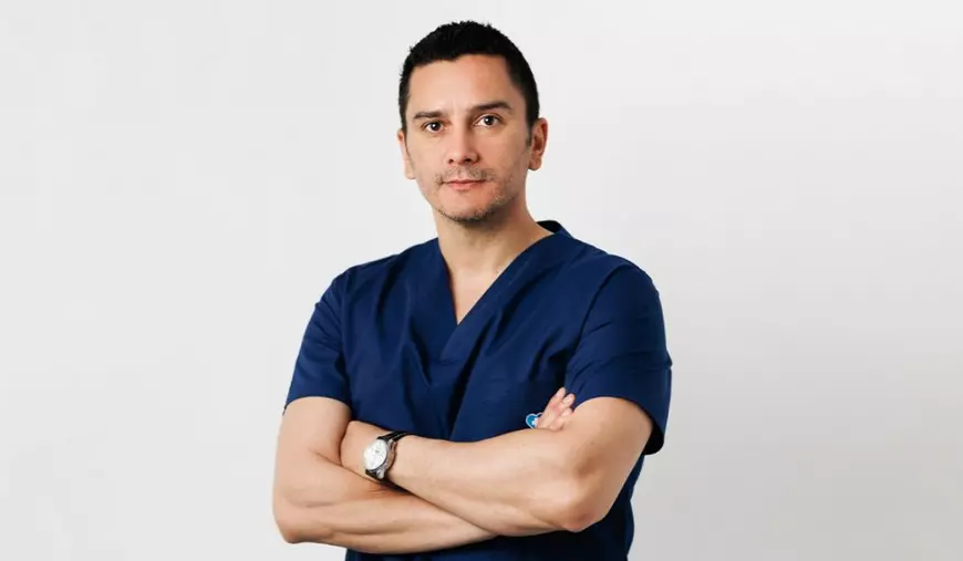 Dr. Gabriel Mitroi, coordonatorul noului Centru de Excelență în Neurochirurgia Pelvină, in bluz[ bleumarin si mainile ]ncricisate la piept, pe fundal alb