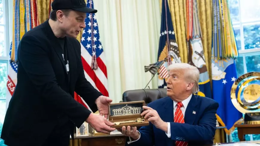 Elon Musk, imbracat în negru, sta în picioare, si primeste un cadou, o cheie de aur, de la Donaldd Trump, care sta pe scaun în Biroul Oval