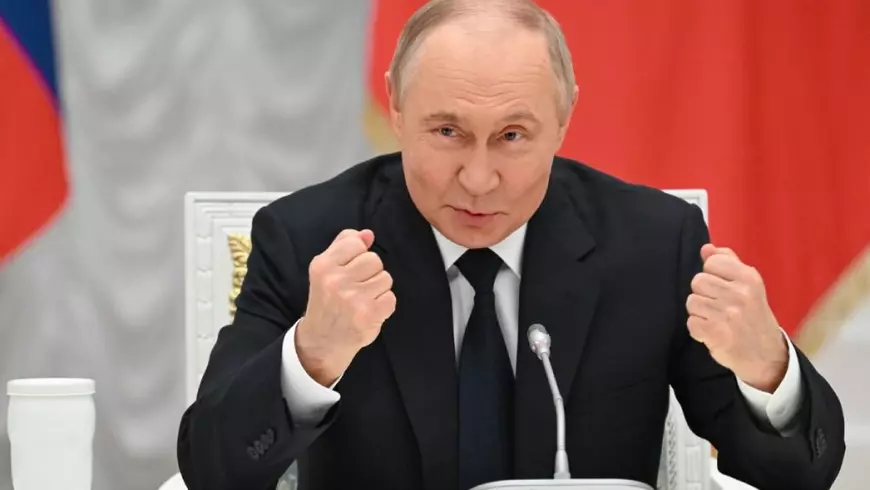 În imagine liderul rus Vladimir Putin, cu mainile ridicare si pumnii strânsi, stând la masă