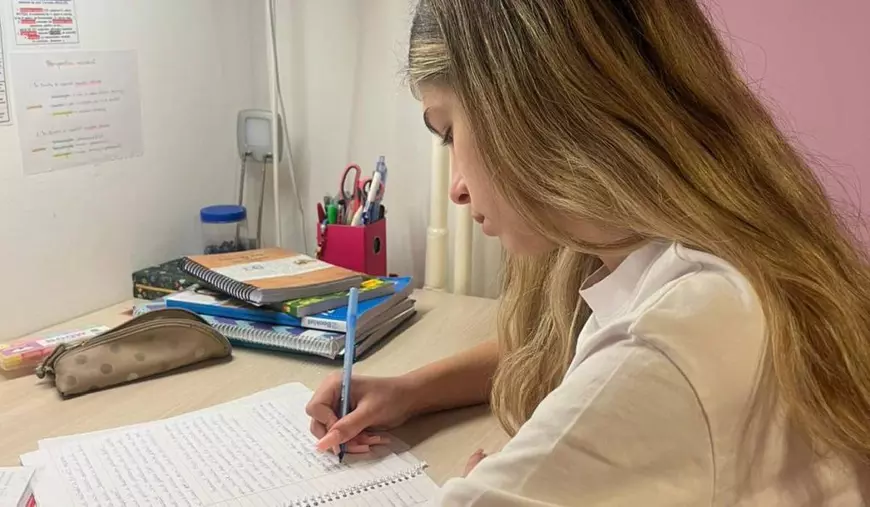 Tânără care stă la birou și scrie cu pixul pe un caiet