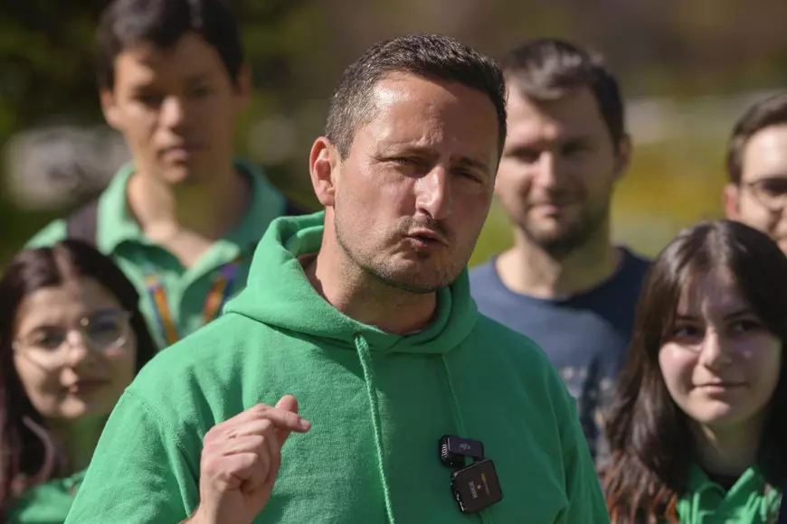 Imagine cu Nicu Ștefănuță vorbind și având o mână ridicată. Acesta poartă un hanorac verde