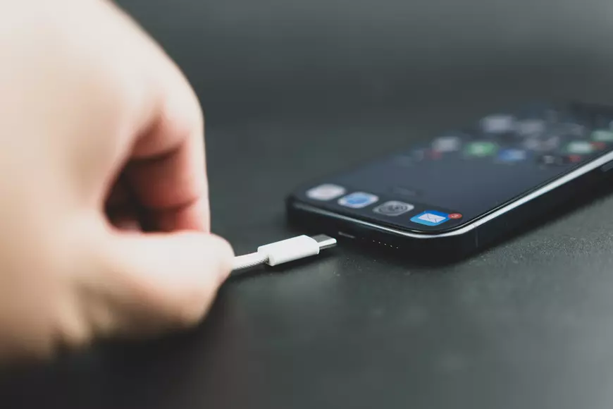 De ce nu este bine să lași telefonul la încărcat noaptea - Imagine în care apare mâna unui bărbat care conectează un cablu de încărcare la un telefon mobil.
