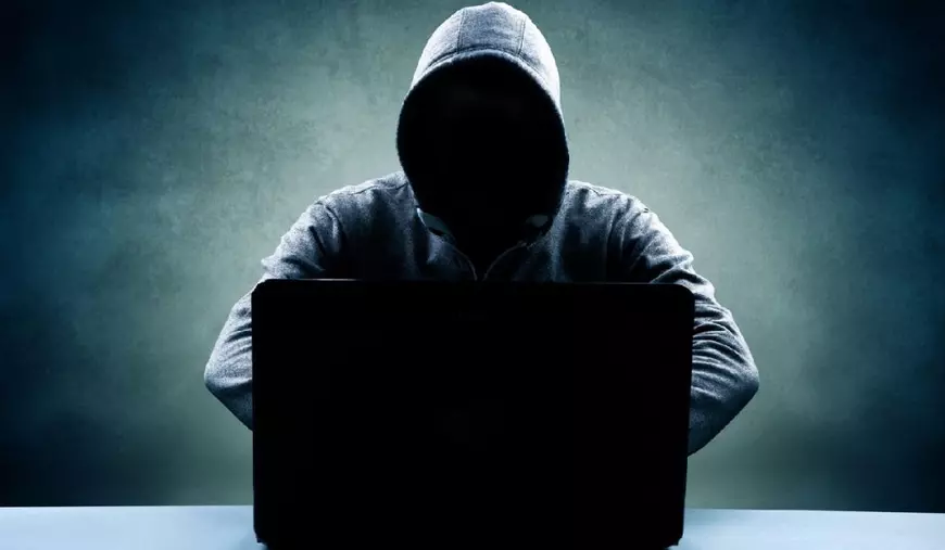 Bărbat în hanorac, cu fața ascunsă, stând în fața unui laptop