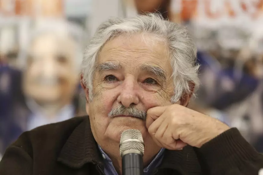 Jose Mujica surprins în timp ce ține o mână la obraz și se află în fața unui microfon. Imagine din aprilie 2016