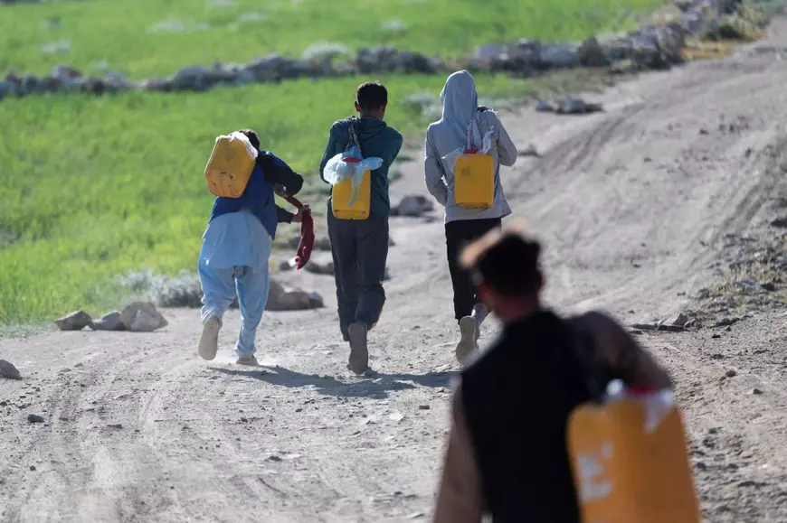 Imagine cu patru oameni pe un drum care cară canistre cu apă potabilă, în Kabul