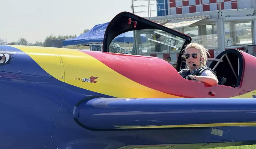 Femeie pilot, în cockpit-ul deschis al unui Extra 300L aflat la sol, în fața hangarului.